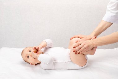 Six month baby girl receiving osteopathic or chiropractic treatment in pediatric clinic. Manual therapist manipulates chils's legs performing exercise for hip dysplasia prevention clipart