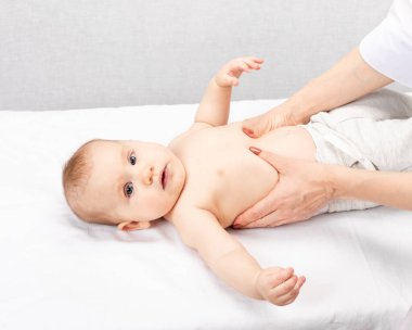 Altı aylık bebek çocuk kliniğinde masaj terapisi görüyor. El terapisti çocuğun karnını ve göğsünü manipüle ediyor.