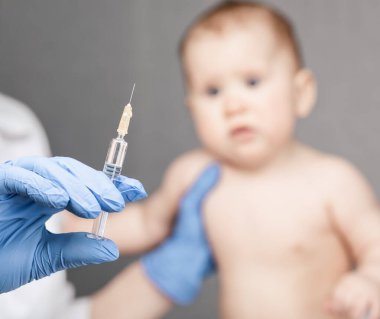 Pediatrician or nurse ready to give an intramuscular injection of a vaccine to a baby girl during coronavirus COVID-19 pandemic
