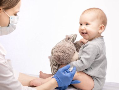 Pediatrician or nurse giving an intramuscular injection of a vaccine to leg of happy baby girl during coronavirus COVID-19 pandemic