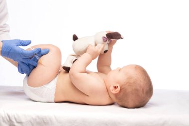 Pediatrician or nurse giving an intramuscular injection of a vaccine to leg of baby girl during coronavirus COVID-19 pandemic
