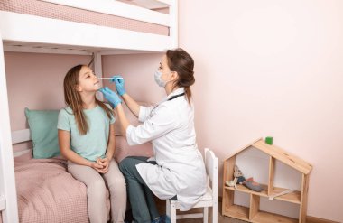 Pediatrician taking nasal mucus test sample from elementary age girl's nose performing respiratory virus testing procedure at home during coronavirus COVID-19 pandemic quarantine