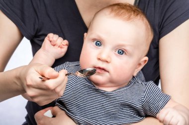 Mother feeding baby boy with vitamin or liquid medicine using spoon