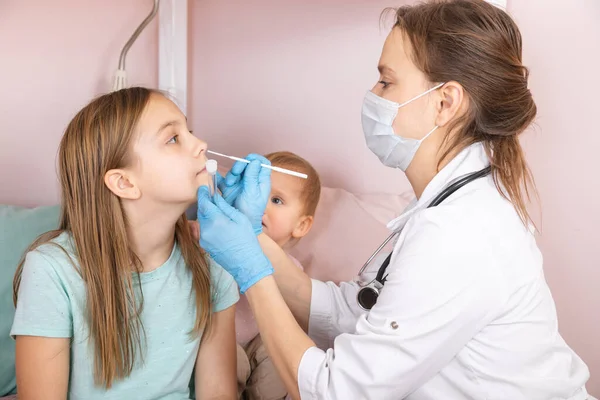 Pediatrician taking nasal mucus test sample from elementary age girl\'s nose performing respiratory virus testing procedure at home during coronavirus COVID-19 pandemic quarantine