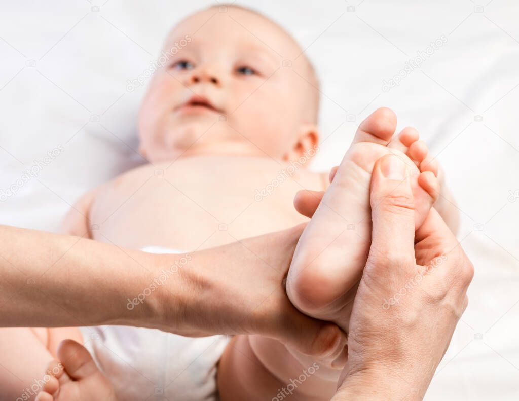 Five month baby boy receiving massage therapy in pediatric clinic. Manual therapist manipulates childs's foot