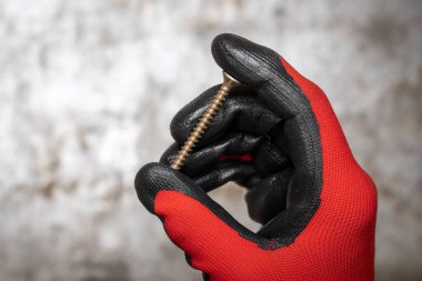 Marangoz koruyucu eldiven giyip paslı metal arka planda sivri uçlu vida tutuyor.