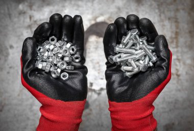 Koruyucu eldivenler giyen biri metal arka planda bir avuç cıvata ve fındık tutuyor.