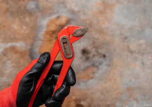 机修工或管道工戴防护手套 手持红色可调钳 以对抗锈蚀的金属底座 — 图库照片