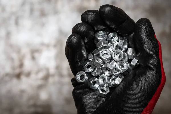 Person Mit Schutzhandschuh Hält Eine Handvoll Muttern Vor Metallischem Hintergrund — Stockfoto