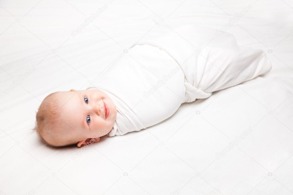 Swaddled infant in white blanket laying on a bed