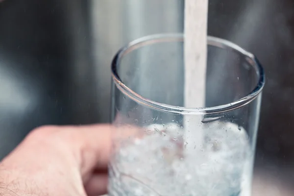Наполнение стакана питьевой водой из кухонного крана — стоковое фото