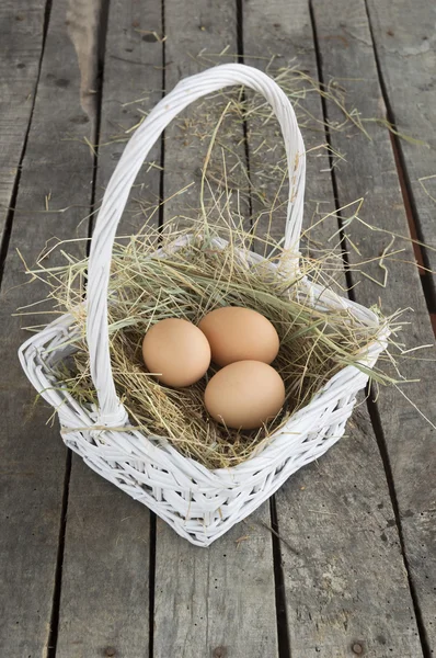 Tre uova su fieno in cesto bianco su fondo di legno — Foto Stock