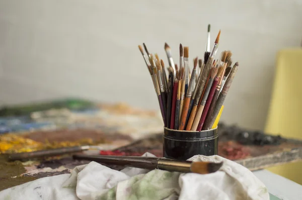 Painting brushes in black jar on plank as a palette — Stock Photo, Image