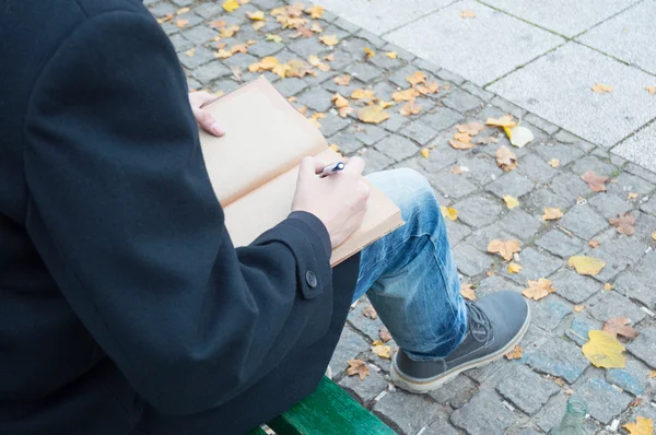 Hombre escribiendo en cuaderno de papel reciclado en su regazo —  Fotos de Stock