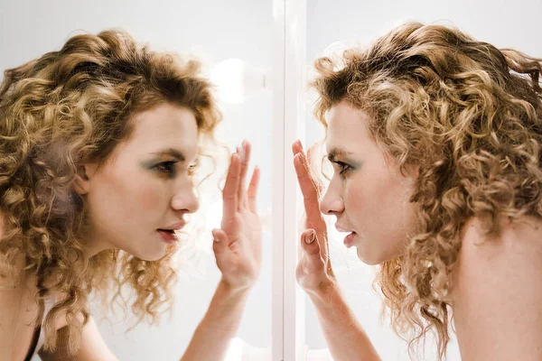 Face in profile with curly blond hair trying to see something thru the mirror. Split personality