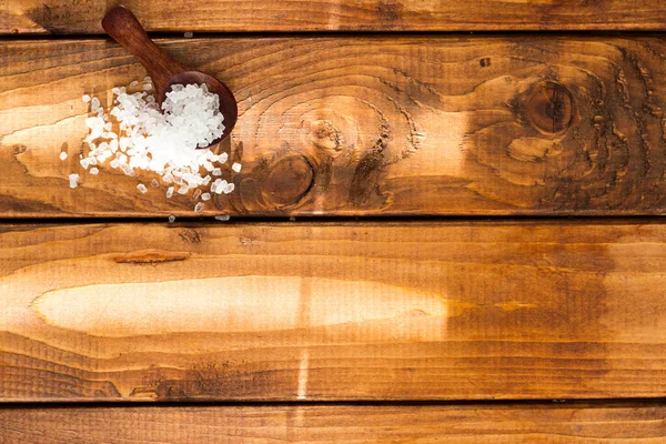 Salt in a wooden spoon on a wooden table. Large pieces of salt in a small wooden spoon on brown boards.