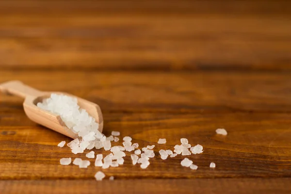 Salt in a wooden spoon on a wooden table. Large pieces of salt in a small wooden spoon on brown boards.