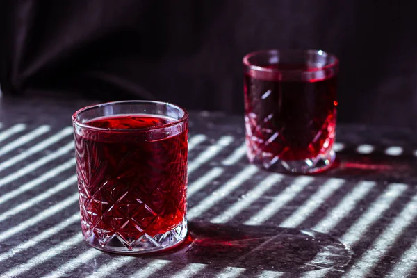 a glasses filled with a red drink stand on a dark background with streaks of light