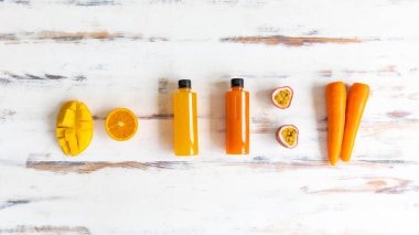 Plastik meyve ve sebze suyu şişelerinin manzarası. Kırsal bir ahşap masanın etrafında elma havucu portakalı ve mango yeri var. Sağlıklı içecekler, detoks ve diyet kavramı.