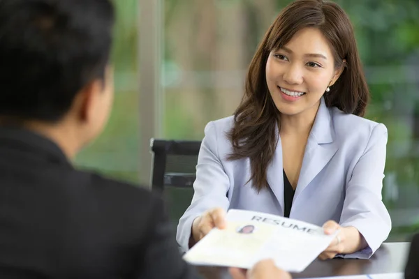 Gülümseyen güzel Asyalı kadının portresi ve özgeçmişini insan kaynakları ofisindeki mülakata vermek. Açık mavi takım giyen güzel adayın seçici odak noktası. İş başvurusu kavramı.