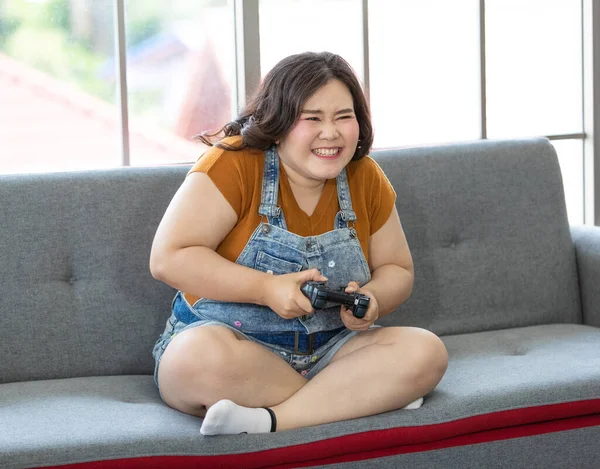 自宅で休日に真剣にゲームをプレイ中に脂肪アジアの女性が座って コンピュータ画面を見てジョイスティックを保持するの肖像画 女性の顔を中心に — ストック写真