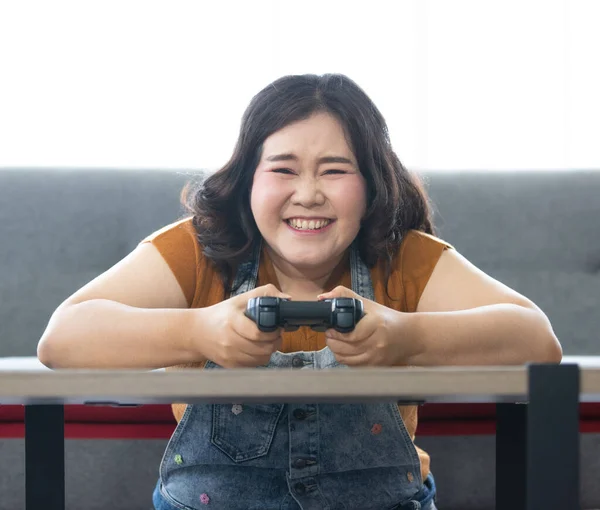 明るい太ったアジアの女性の肖像が座っていると幸福と自宅で休日にコンピュータゲームをプレイ中にカメラを見てジョイスティックを保持します 女性の顔を中心に — ストック写真
