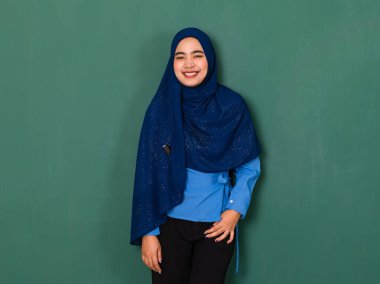 Mutlu gülümseyen genç bir kadının portresi. Güzel giyinmiş, mavi tesettürlü, yeşil arka planda duran ve kameraya bakan güzel bir Müslüman kadın..