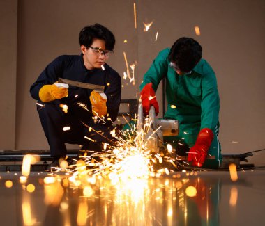 Takım çalışması, güvenlik çalışması konsepti. Bir fabrikanın atölyesinde çalışan bir mühendis. Tamirci elbisesi güvenliği bir metali kesmek için kesici alet kullanır. Demir kesmenin kıvılcımı..