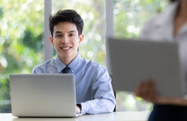 İşadamı dizüstü bilgisayarla masada oturuyor ve kameraya gülümsüyor..