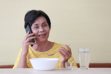 Asyalı yaşlı kadın yemek tabağıyla oturuyor.