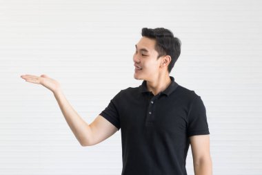 Siyah gömlekli yakışıklı ve yakışıklı bir Asyalı güçlü ve enerjik poz veriyor. Elleri reklamlara benziyor ve bir şeyler gösteriyor..