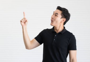 Siyah gömlekli yakışıklı ve yakışıklı bir Asyalı güçlü ve enerjik poz veriyor. Heyecanla parmaklarını havaya kaldırır..