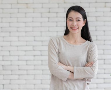 Güzel, güzel bir melez ırkın portresi. Asyalı yetişkin bir kadın. Kollarını kavuşturmuş, kendine güvenen ve arkadaş canlısı bir şekilde kameraya poz veriyor.