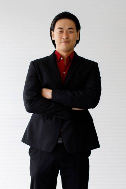 Resim bir portredir. Mutlu ve gülümseyen Asyalı işadamı, siyah takım elbiseli, beyaz bir geçmişle stüdyoda.