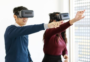 Yakışıklı gülümseyen Asyalı aşık çiftin portresi sanal gerçeklik gözlükleriyle yeni bir video oyunu oynayarak eğleniyor. Sanal dünyada ekrana dokunmaya çalışır gibi dururlar.