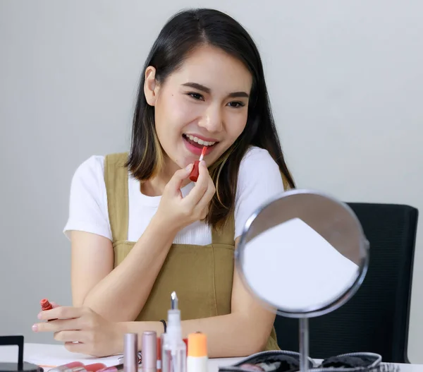 Beauty bloggers present beauty cosmetics while sitting in front camera. Smiling Asian beautiful woman experimenting with red lipstick Apply around the mouth and look in the mirror