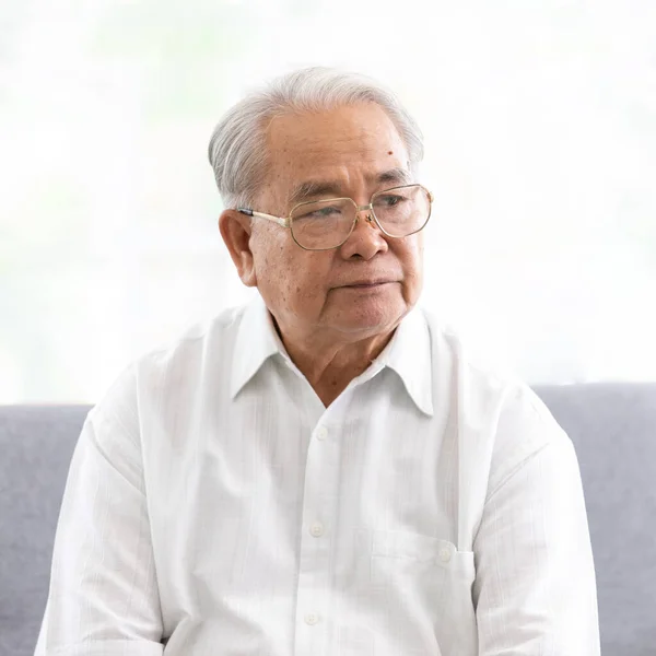 Portrait of old senior asian man wearing eyesglasses and white shirt sitting on sofa