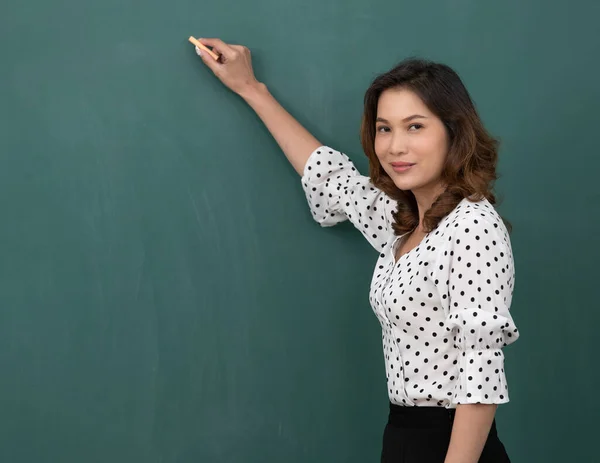 Güzel Asyalı kadın elinde tebeşirle kara tahtanın önünde duruyor..