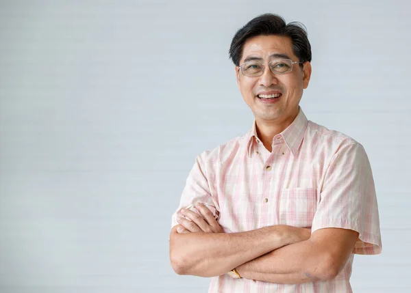 Sıcak kişilik portresi kıdemli gözlük takan, gülümseyen, kollarını kavuşturan yaşlı bir adam kendine güvenen ve iyi görünümlü bir kameraya poz veriyor..