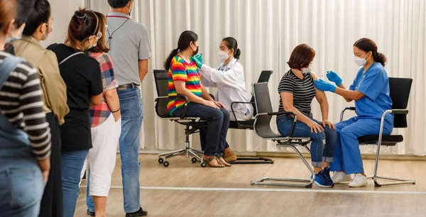 Variety ages citizens standing in a row and waiting for a vaccine injection while medical people injecting to senior women in face mask. Covid-19 or coronavirus  herd immunity concept.