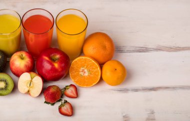 Bardakta, elmada, portakalda ve çilek suyunda farklı meyveler, samanla birlikte beyaz arka planda renkli ahşap tahtada canlandırıcı görünüyor. Taze meyvelerle süsleme.