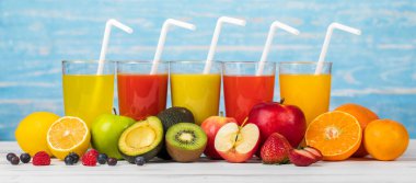 Bardakta, elmada, portakalda ve çilek suyunda farklı meyveler, samanla birlikte mavi arka planda renkli ahşap tahtada canlandırıcı görünüyor. Taze meyvelerle süsleme.