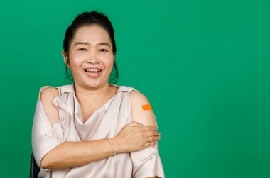 Kolunda bandaj bandı olan Asyalı orta yaşlı bir kadın yeşil arka planda Covid 19 virüsü aşısı olduğunu gösteriyor. Covid 19 aşısı için kavram.