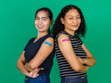 Kollarını bandajlı gösteren iki orta yaşlı Asyalı kadın yeşil arka planda Covid 19 virüsü için aşı olduklarını gösteriyor. Covid 19 aşısı için kavram.