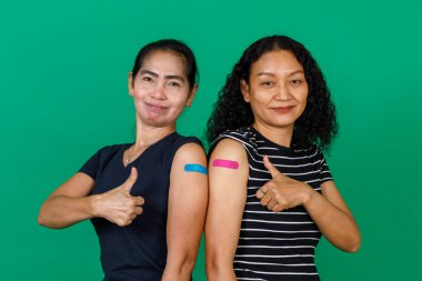 Kollarını bandajlı gösteren iki orta yaşlı Asyalı kadın yeşil arka planda Covid 19 virüsü için aşı olduklarını gösteriyor. Covid 19 aşısı için kavram.