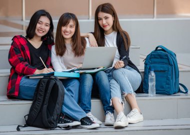 Üç çekici Asyalı kız üniversite öğrencisinden oluşan bir grup dışarıda üniversite kampüsünde dizüstü bilgisayar kullanarak birlikte çalışıyorlar. Eğitim, arkadaşlık ve üniversite öğrencilerinin hayatı kavramı.