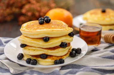 Tatlı yemek. Yaban mersinli ve ballı bir yığın leziz krep, çay, arka planda beyaz tabakta ekose kumaş.