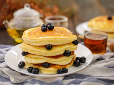 Tatlı yemek. Yaban mersinli ve ballı bir yığın leziz krep, çay, arka planda beyaz tabakta ekose kumaş.
