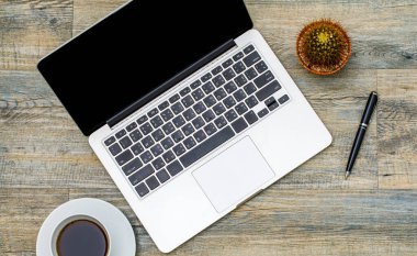 Dizüstü bilgisayarın üst görüntüsü, beyaz fincanda sade kahve ve ahşap desenli arka planda küçük kaktüs tenceresi ile fotokopi alanı..