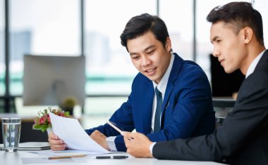 Memnuniyetle Asyalı erkek yöneticiler masada oturup birlikte tablet kullanırken işyerindeki yeni projeden bahsediyorlar.